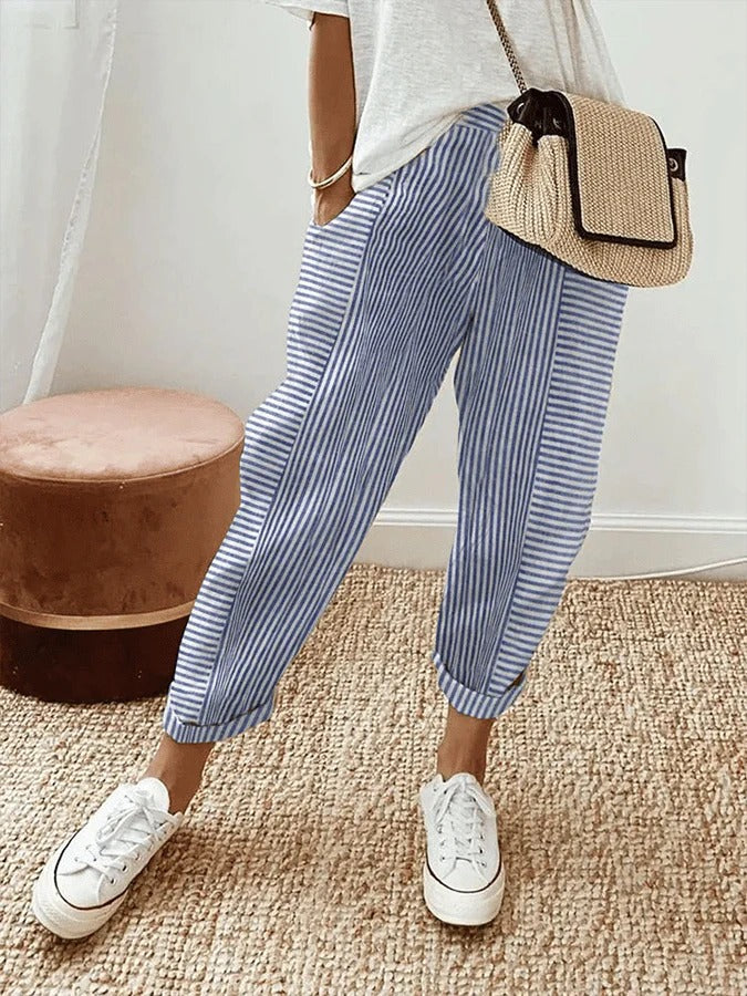 Pantalon rayé bleu et blanc, style décontracté, porté avec un t-shirt blanc, baskets blanches et sac en osier. Mode estivale tendance.