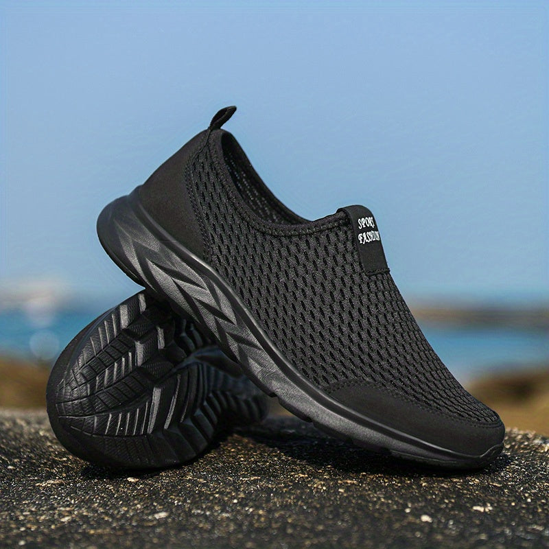 Chaussure de sport noire en maille respirante sur fond de plage, semelle antidérapante, idéale pour la course et les activités extérieures.
