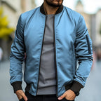 Homme portant un blouson bomber bleu, col noir, manches longues, sur un pull gris, en ville. Mode masculine, style urbain, tendance automne.