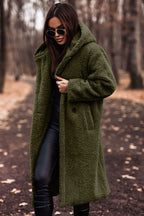 Femme portant un manteau en fausse fourrure vert olive, lunettes de soleil noires, dans un parc automnal. Mode hiver, style chic, tendance.