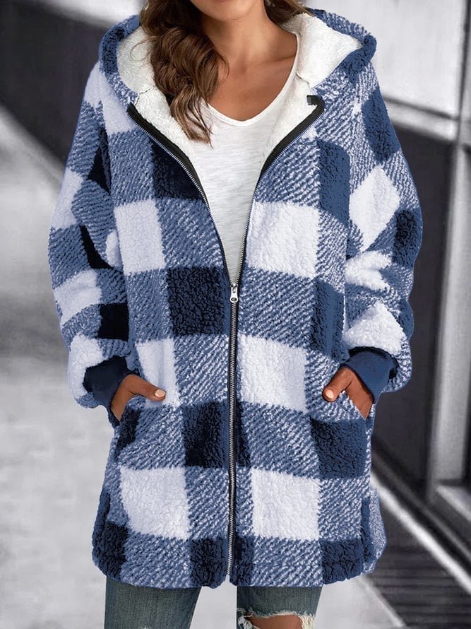 Femme portant un manteau à carreaux bleu et blanc, style décontracté, avec capuche et poches, sur fond urbain. Mode automne-hiver tendance.