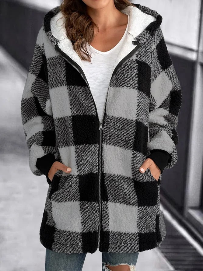 Femme portant un manteau à carreaux noir et blanc, style décontracté, avec capuche et poches, sur fond urbain flou. Mode automne-hiver tendance.