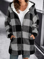 Femme portant un manteau à carreaux noir et blanc, style décontracté, avec capuche et poches, sur fond urbain flou. Mode automne-hiver tendance.