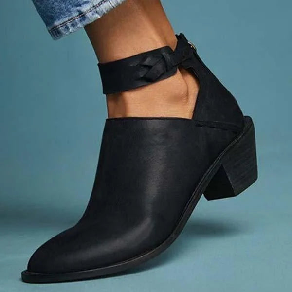 Bottine noire en cuir avec talon carré, design découpé et bride tressée à la cheville, posée sur fond bleu. Chaussure tendance pour femme.