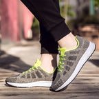 Chaussures de sport grises et vertes pour homme, semelle blanche, portées en extérieur. Sneakers légères, idéales pour la course et le fitness.