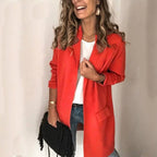 Femme souriante portant un manteau rouge élégant, chemise blanche, jeans, tenant un sac noir. Mode automne, style décontracté chic.