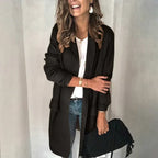 Femme souriante portant un manteau noir élégant, un jean bleu et un sac à main noir. Mode automne, style chic décontracté.
