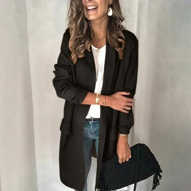 Femme souriante portant un manteau noir élégant, un jean bleu et un sac à main noir. Mode automne, style chic décontracté.