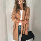 Femme souriante portant un manteau camel élégant, t-shirt blanc, jeans, tenant un sac noir. Mode automne chic, style décontracté tendance.