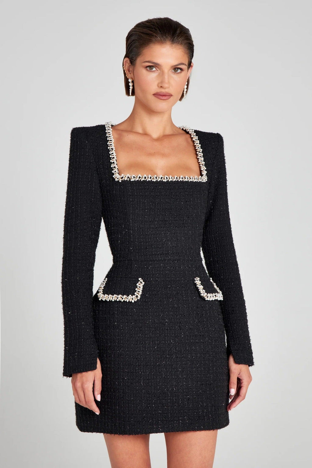 Robe noire élégante en tweed avec col carré et bordures perlées, manches longues, poches décoratives, portée par une femme. Mode chic et sophistiquée.