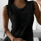 Femme portant une élégante robe en dentelle noire avec motifs floraux, tenant un sac à main noir à chaîne dorée, sur fond de salon moderne.