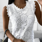 Femme portant un haut en dentelle blanche avec motifs floraux, tenant un sac à main noir à chaîne dorée. Mode élégante, tenue chic, style féminin.
