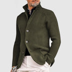 Homme portant un cardigan en maille vert olive avec boutons, col relevé, chemise noire et pantalon blanc. Mode masculine élégante et moderne.