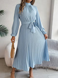 Robe midi plissée bleu clair avec manches longues et ceinture nouée, tenue élégante pour femme, accessoirisée d'un sac en osier.