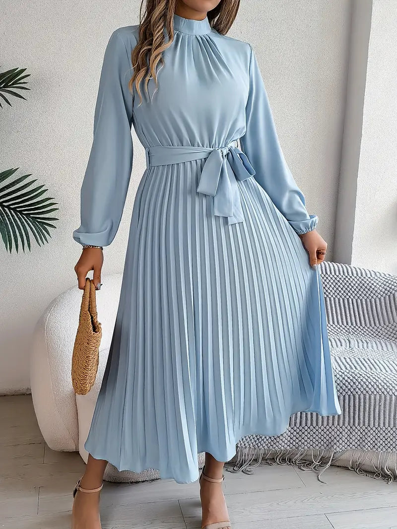 Robe midi plissée bleu clair avec manches longues et ceinture nouée, tenue élégante pour femme, accessoirisée d'un sac en osier.