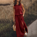 Femme en robe longue rouge, chapeau de paille, sandales blanches, portant un sac en osier, marchant dans un champ en été. Mode estivale élégante.