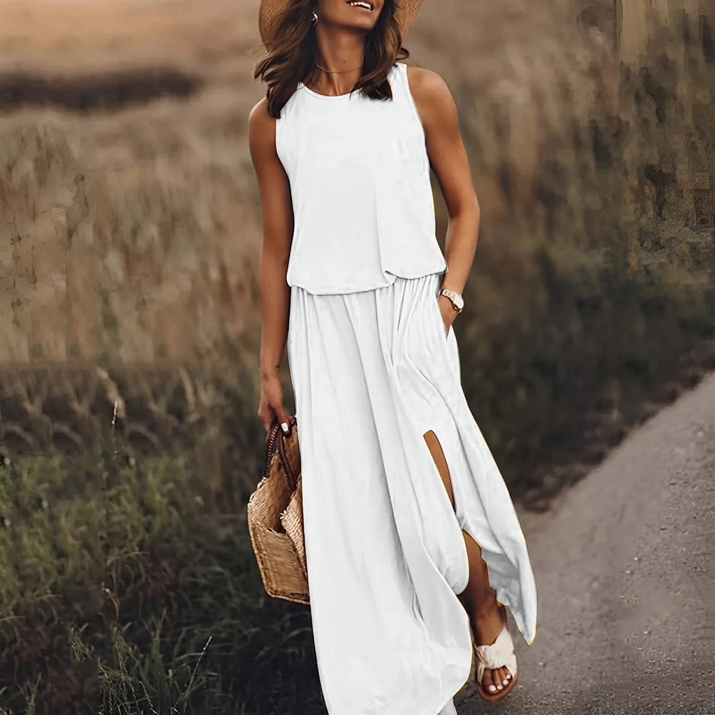 Femme en robe blanche d'été, chapeau de paille, sandales, tenant un sac en osier, marchant sur un chemin rural. Mode estivale élégante.