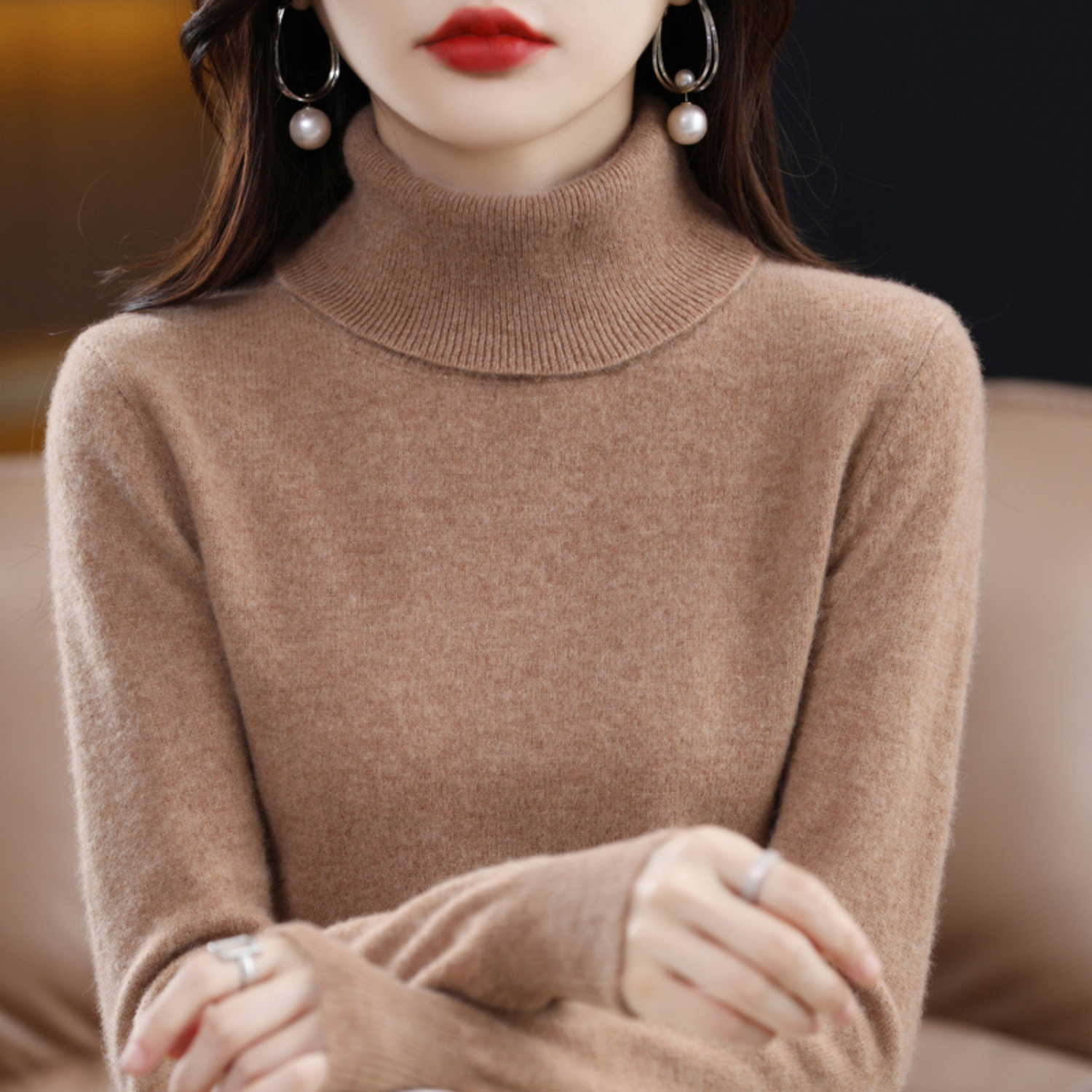 Femme portant un pull col roulé beige, boucles d'oreilles pendantes avec perles, lèvres rouges. Mode automne-hiver, élégance féminine.