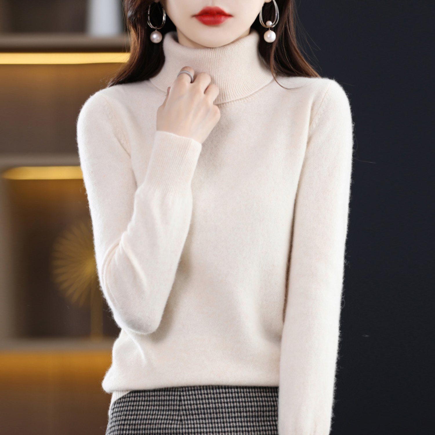 Femme portant un pull col roulé blanc, élégant et moderne, avec des boucles d'oreilles perle, mode automne-hiver, style chic et tendance.