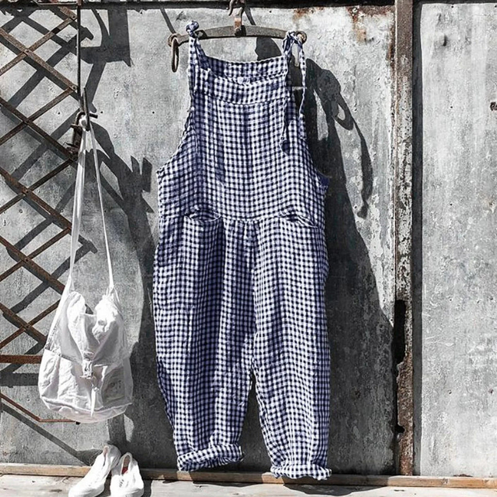 Salopette à carreaux bleus et blancs suspendue à un mur en métal vieilli, accompagnée d'un sac blanc et de chaussures blanches. Mode vintage décontractée.