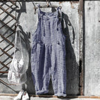 Salopette à carreaux bleus et blancs suspendue à un mur en métal vieilli, accompagnée d'un sac blanc et de chaussures blanches. Mode vintage décontractée.