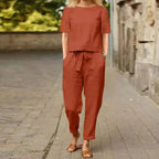 Femme en ensemble décontracté en lin rouge brique, marchant sur une rue pavée. Mode estivale, tenue confortable, style urbain chic.
