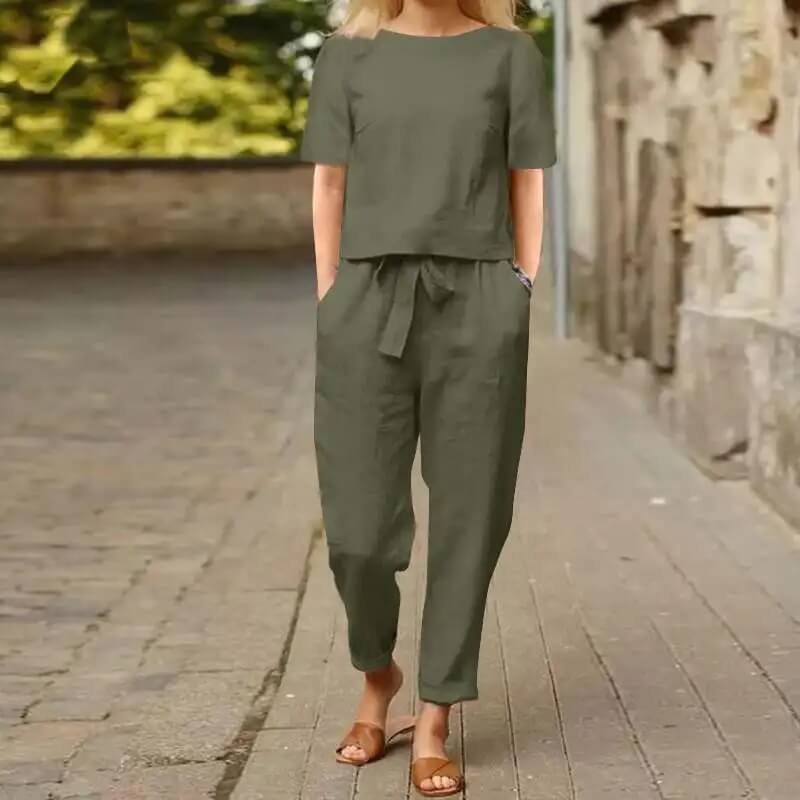 Femme en combinaison kaki, manches courtes, marchant sur un trottoir pavé, portant des sandales marron. Mode décontractée, tenue estivale élégante.