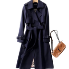 Manteau trench-coat bleu marine élégant avec ceinture, boutons et détails épaulettes, accompagné d'un sac à main en cuir marron. Mode automne chic.