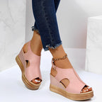 Sandales compensées roses pour femme avec talons en liège, portées avec un jean bleu déchiré à la cheville, sur fond blanc marbré.