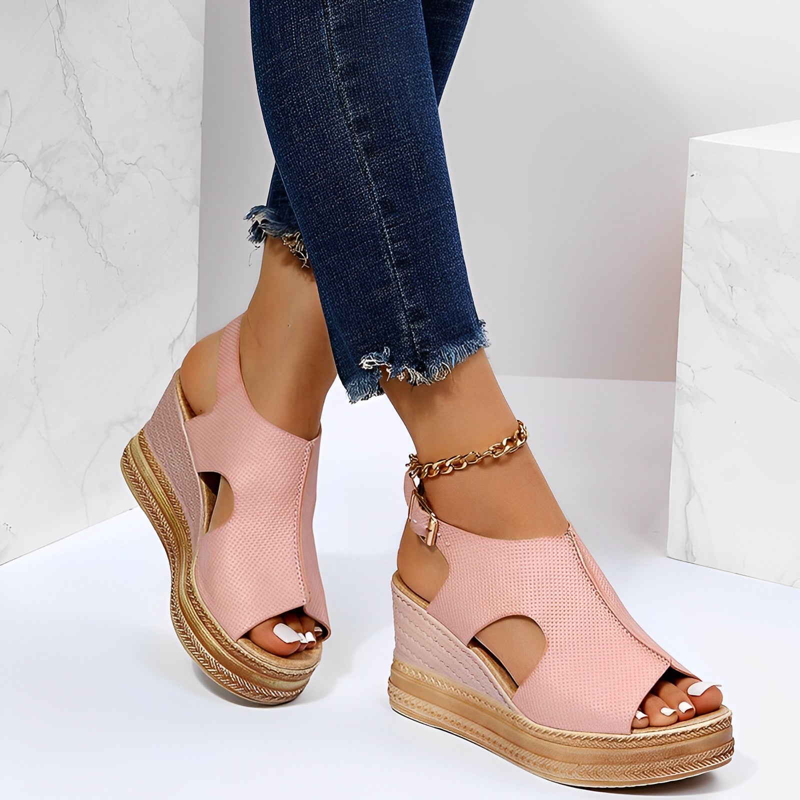 Sandales compensées roses pour femme avec talons en liège, portées avec un jean bleu déchiré à la cheville, sur fond blanc marbré.