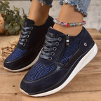 Chaussures de sport bleu marine pour femme avec lacets, détails en strass, fermeture éclair latérale, portées avec un jean déchiré et bracelet perlé coloré.