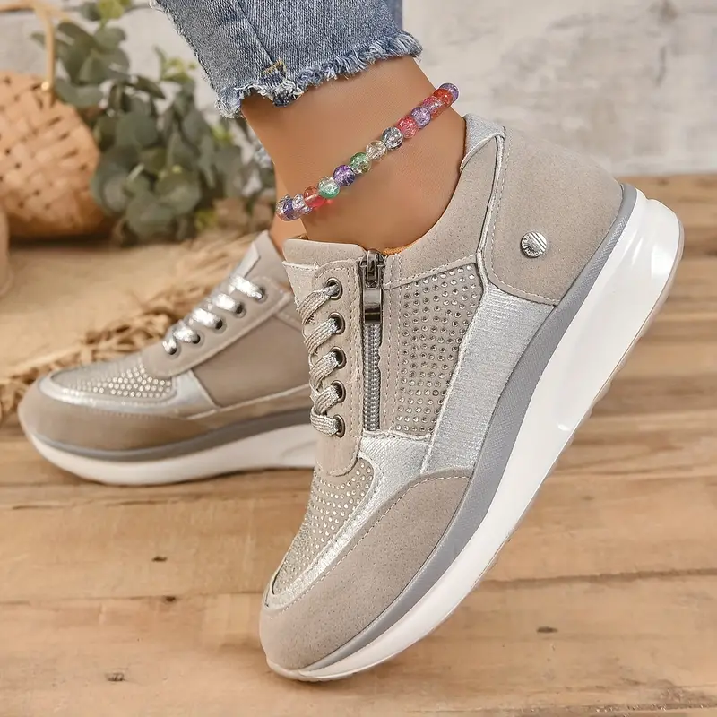 Chaussures de sport beiges pour femme avec semelle compensée, détails brillants et fermeture éclair latérale, portées avec un bracelet de cheville coloré.