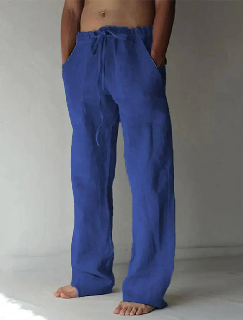 Homme portant un pantalon ample bleu en lin, pieds nus, avec poches et cordon à la taille. Mode décontractée, confort, style estival.
