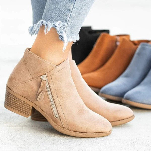 Bottines beiges en daim avec fermeture éclair, portées avec un jean déchiré, entourées de bottines marron, noires et bleues. Mode automne-hiver.