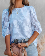 Blouse en dentelle blanche à manches bouffantes, portée avec un jean bleu clair. Sac à main beige en cuir souple. Mode féminine élégante et tendance.