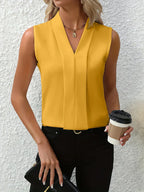 Femme en haut jaune sans manches, tenant un café à emporter et un sac noir, posant devant un mur blanc texturé. Mode élégante et décontractée.