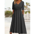 Robe longue noire élégante avec manches courtes, col en V croisé, poches latérales, portée par une femme en extérieur. Mode féminine chic.