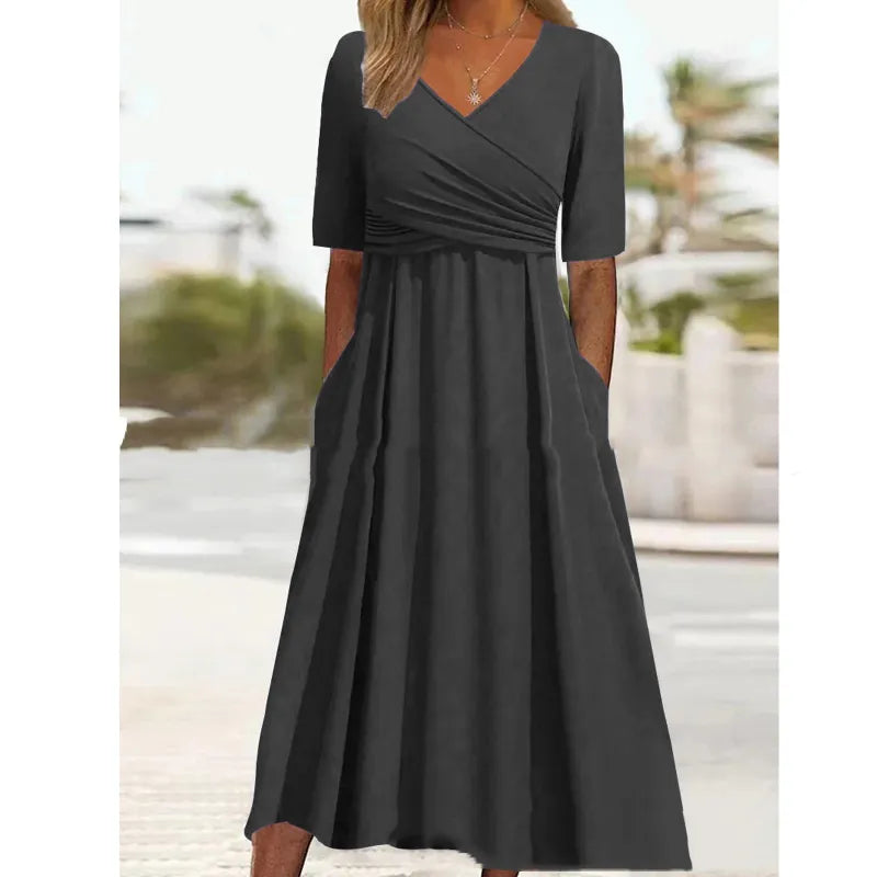 Robe longue noire élégante avec manches courtes, col en V croisé, poches latérales, portée par une femme en extérieur. Mode féminine chic.