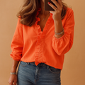 Femme portant une chemise orange à volants, manches longues, avec un jean bleu. Style décontracté, mode féminine tendance, fond beige.