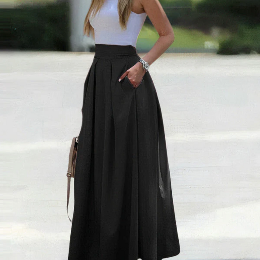 Femme en jupe longue noire élégante, haut blanc sans manches, posant à l'extérieur. Mode féminine chic, tenue estivale tendance.