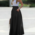 Femme en jupe longue noire élégante, haut blanc sans manches, posant à l'extérieur. Mode féminine chic, tenue estivale tendance.