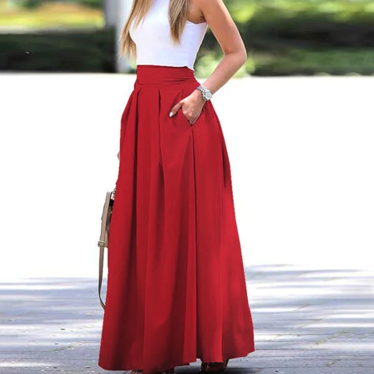 Femme en jupe longue rouge élégante, haut blanc sans manches, tenant un sac à main beige, mode estivale chic, style décontracté.