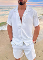 Homme en chemise blanche en lin sur plage au coucher du soleil, style estival décontracté, mode masculine, bord de mer, tenue élégante.