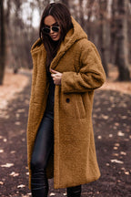 Femme portant un manteau en fausse fourrure marron, lunettes de soleil, pantalon noir, marchant dans un parc automnal. Mode hiver, style urbain.