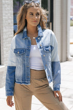 Femme portant une veste en jean patchwork, t-shirt blanc et pantalon beige, posant à l'extérieur. Mode décontractée, tendance urbaine, style moderne.