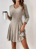 Robe tricotée beige à manches longues, col en V, tenue par une femme avec un gobelet à café. Mode automne, style décontracté et élégant.