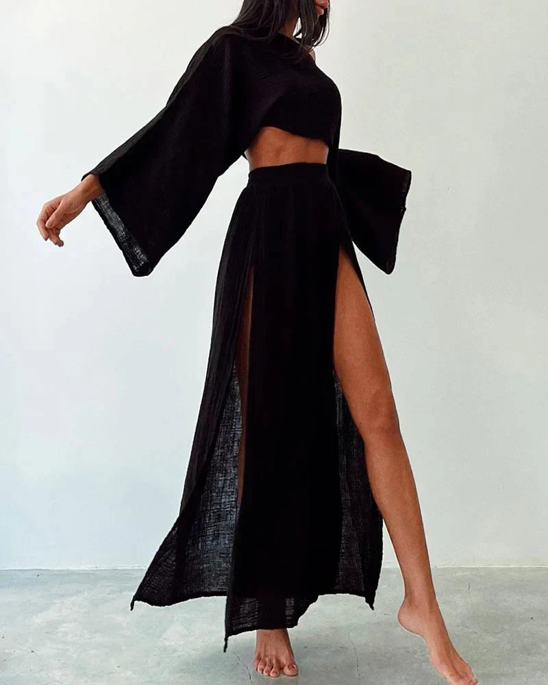 Femme portant une robe noire élégante avec manches longues et fente haute, mode minimaliste, style chic et moderne, fond neutre.