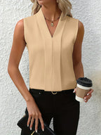Femme en haut sans manches beige, tenant un café à emporter et une pochette noire, posant devant un mur blanc texturé. Mode élégante et décontractée.