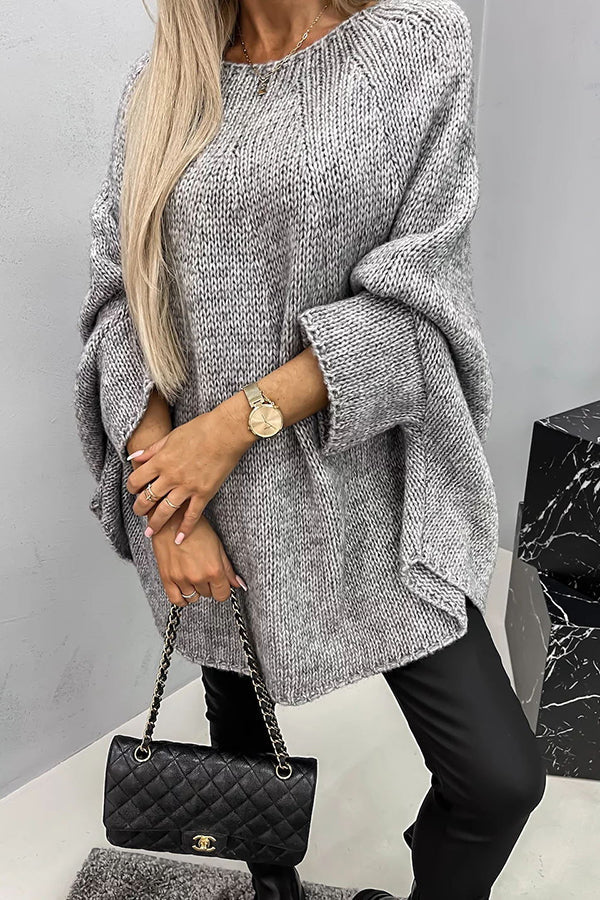 Femme portant un pull oversize gris en tricot, tenant un sac à main noir matelassé. Mode automne-hiver, style décontracté chic.