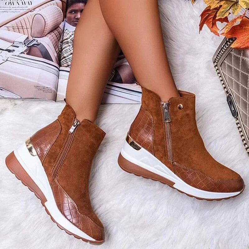 Bottes marron en daim avec fermeture éclair, semelle blanche et détails en cuir croco, posées sur un fond automnal avec magazine et sac à main.